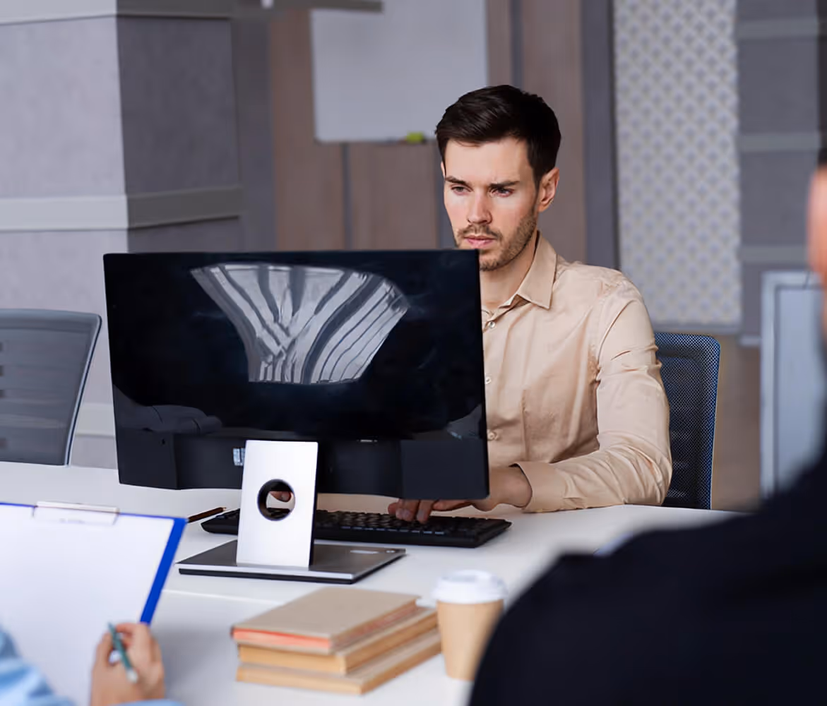 Mann konzentriert bei der Arbeit am Computer an einem Büroraumtisch mit Kaffeetasse und Büchern.