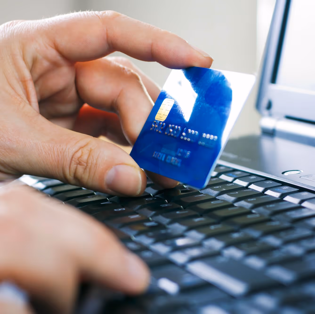 Hand hält blaue Kreditkarte über Laptop-Tastatur für Online-Zahlung.