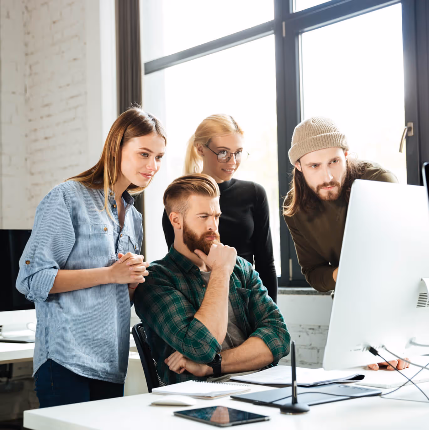 Vier junge Kollegen konzentrieren sich auf einen Computermonitor in einem hellen Büro.