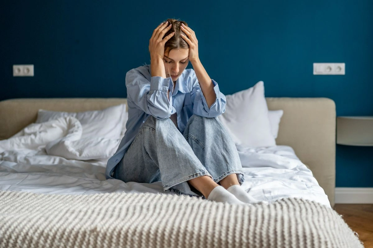 A stressed lady sitting on bed and holding her head