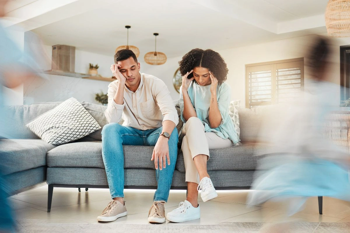 Stressed parents sitting on sofa while their kids are running around