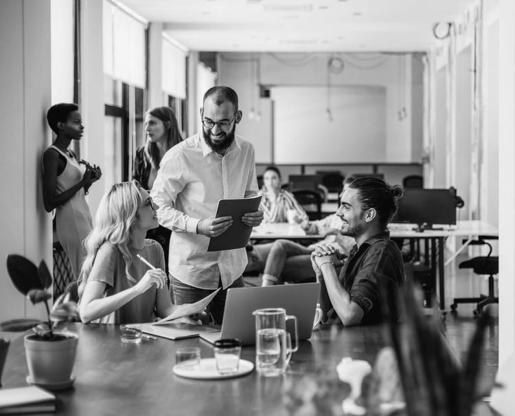 Група молодих людей обговорює проєкт в сучасному офісі з ноутбуком і документами на столі.