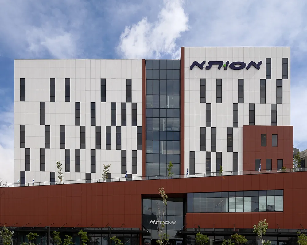 Modern office building with white and brown facade featuring vertical rectangular windows and a blue sky background.