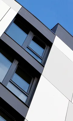 Modern building facade with black-framed windows and white panels under a clear blue sky.