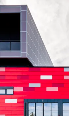 Modern building with a red facade featuring rectangular patterns and large windows, topped by a gray cubic structure with grid lines.