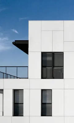 Section of modern white building facade with black-framed windows against a clear blue sky.