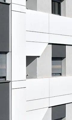 Modern building facade with white panels and windows partially covered by gray shutters casting geometric shadows.