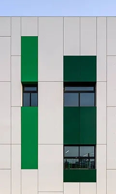 Modern building facade with vertical green panels and rectangular windows against a light beige wall under clear sky.