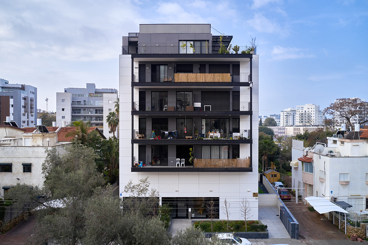 Modern mid-rise apartment building with balconies and rooftop garden set against a partly cloudy sky.
