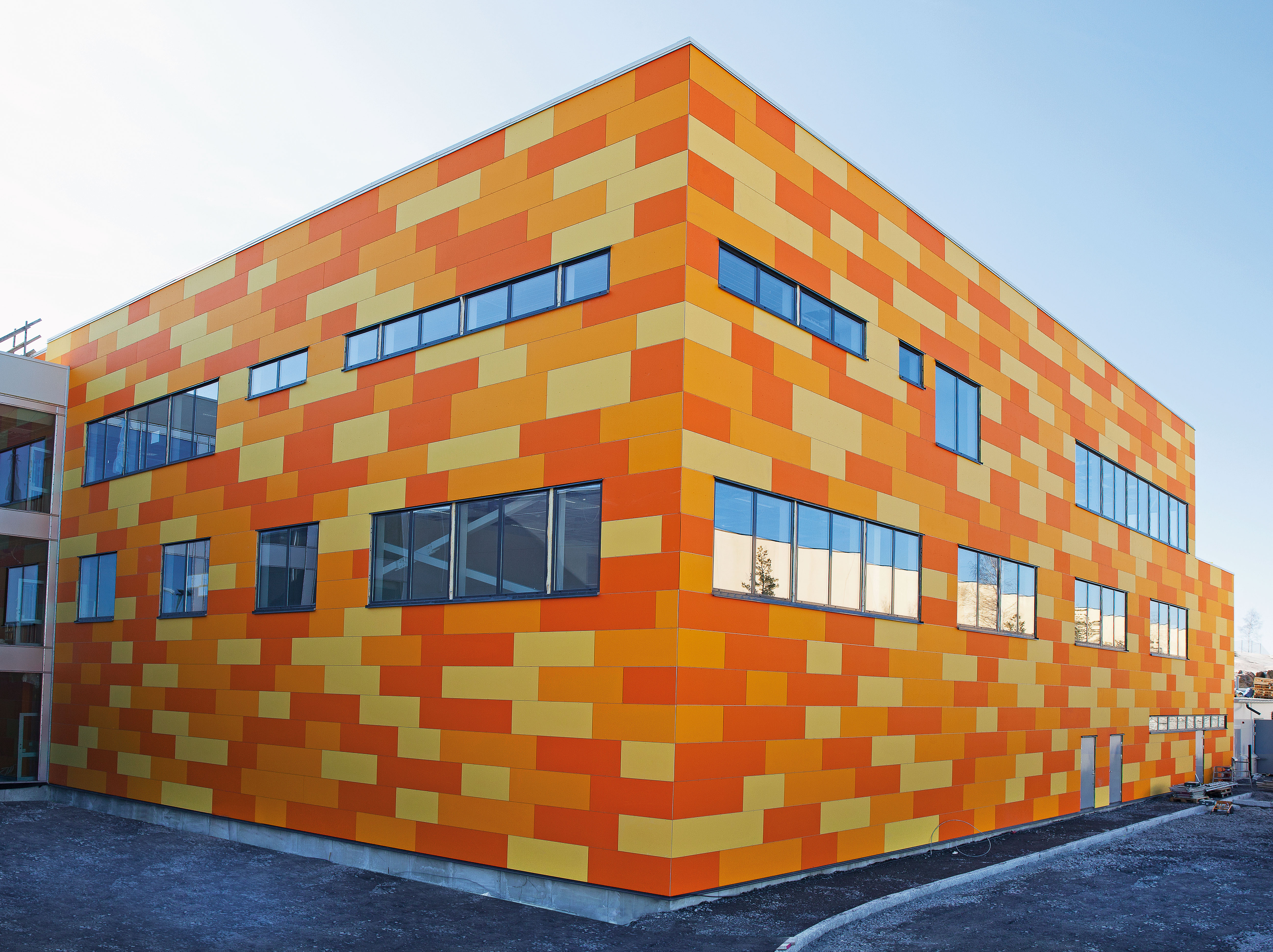 Modern building with a façade of orange and yellow rectangular panels and multiple horizontal windows reflecting the sky.