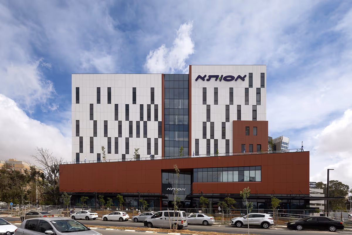 Modern office building with white and red exterior panels and vertical windows under a partly cloudy sky.