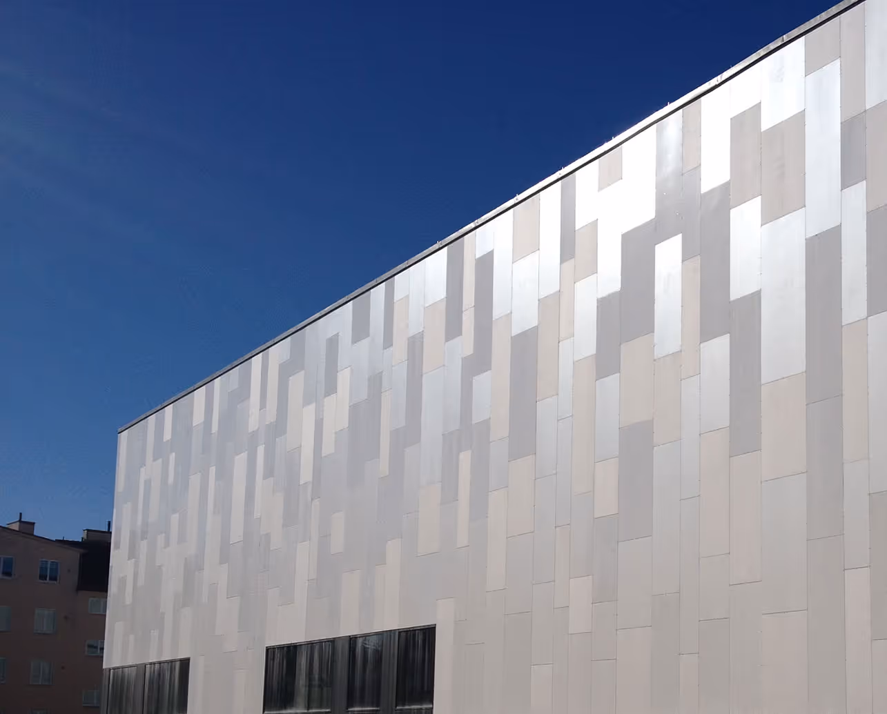 Modern building facade with a pattern of light and dark rectangular panels under a clear blue sky.