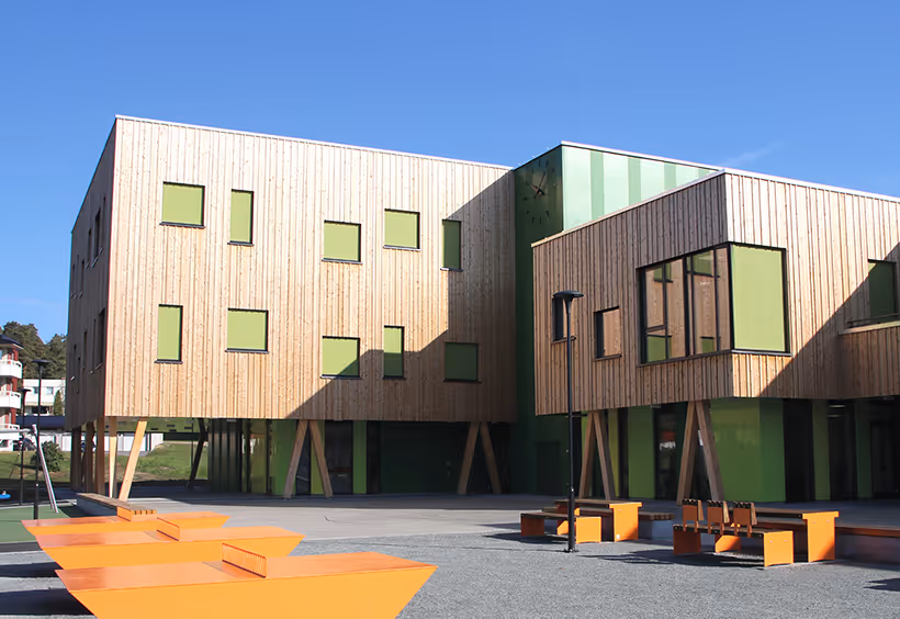 Modern two-story wooden building with green window panels and outdoor orange seating under a clear blue sky.