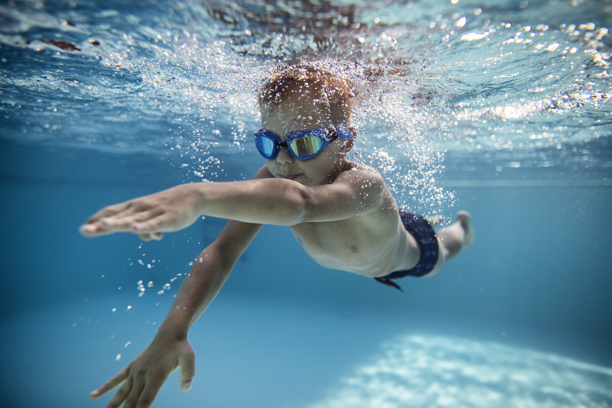 Kind mit Schwimmbrille beim Schwimmen unter Wasser im Schwimmkurs