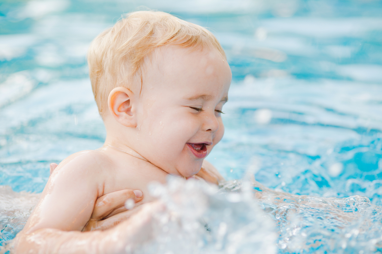 Fröhliches Baby genießt spielerisch das Wasser beim Babyschwimmen