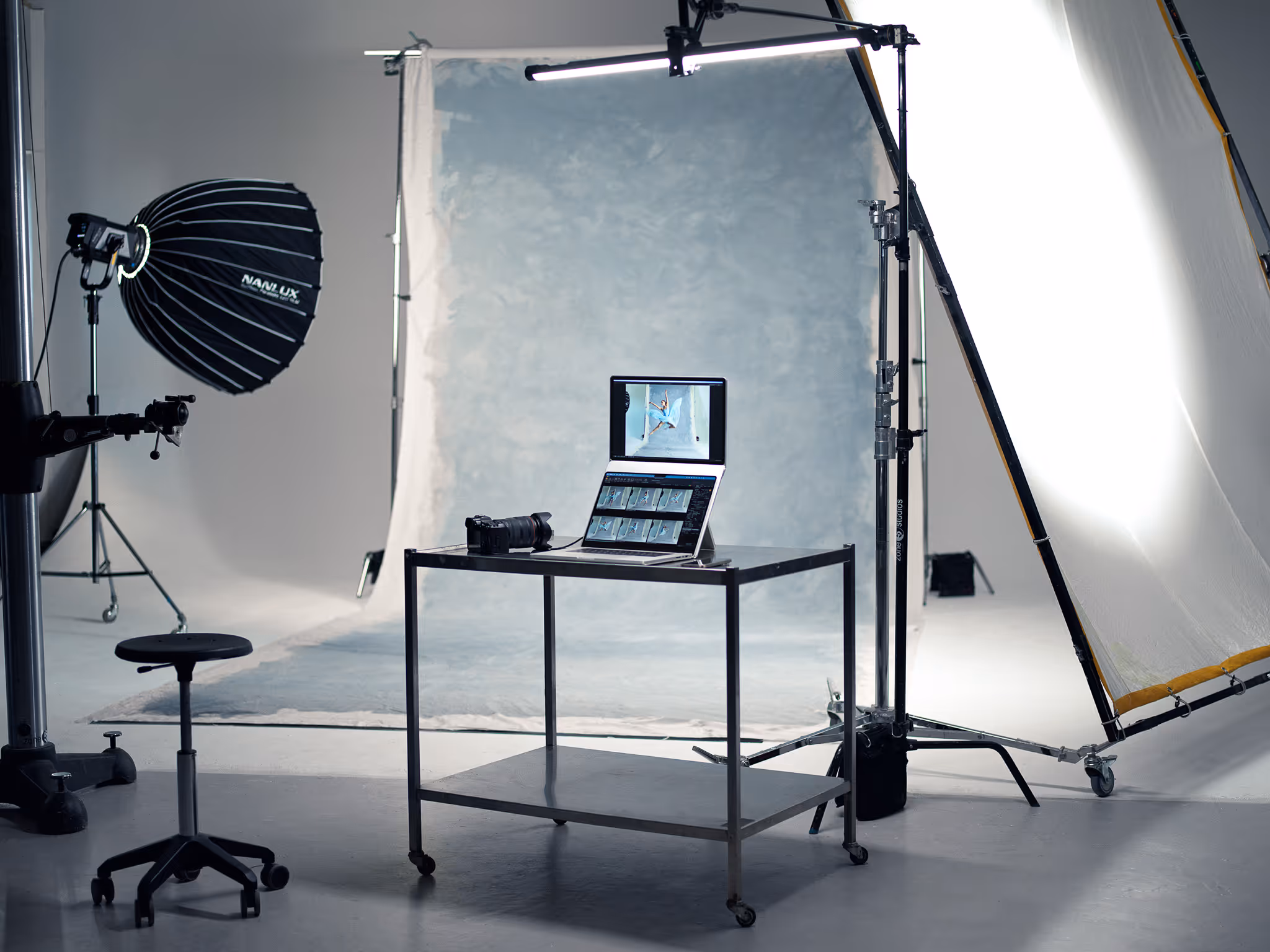 Modern photography studio setup with lighting equipment, backdrop, a laptop on a metal table displaying photo edits, and a camera.