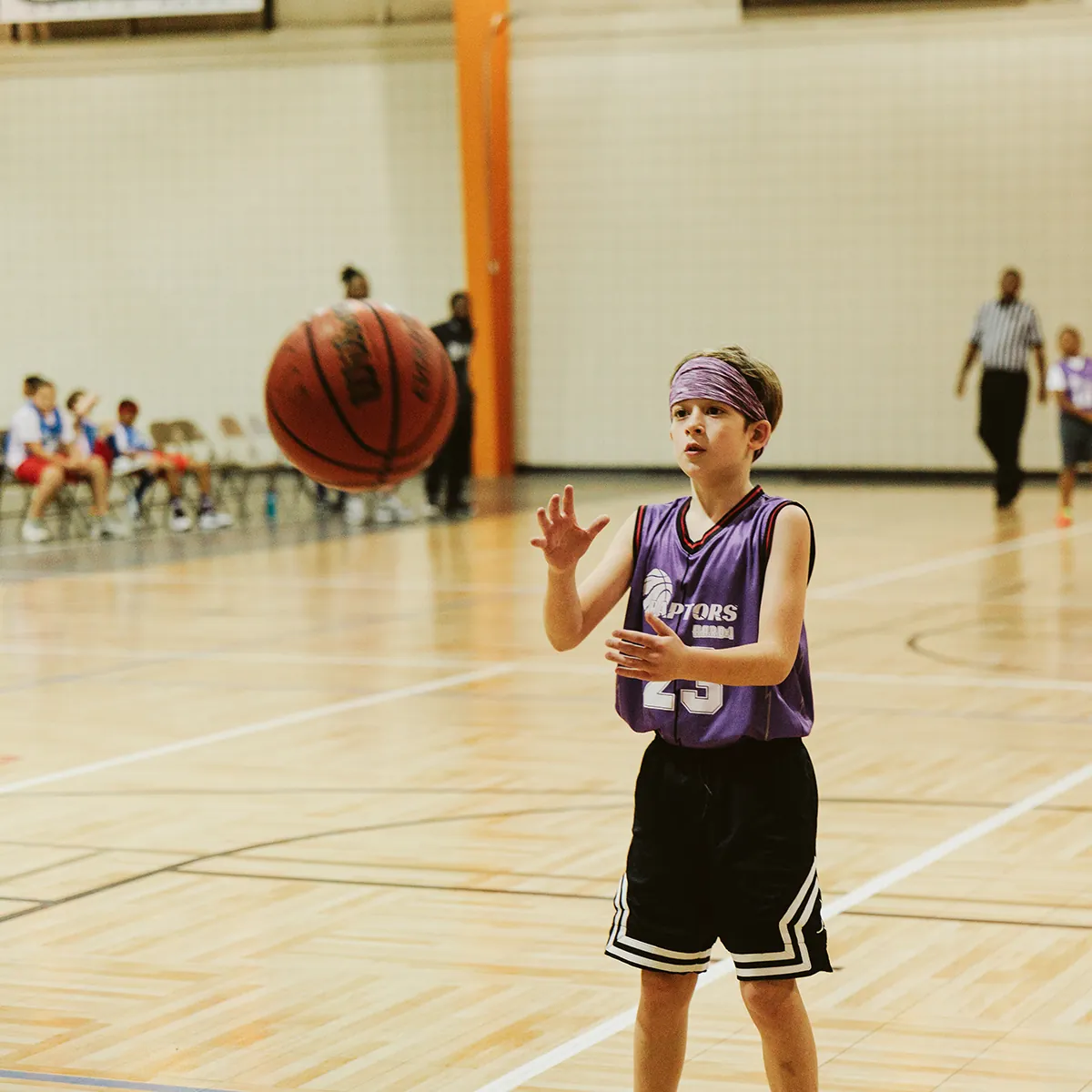 Young basketball player in H.A.R.D. #1 purple jersey catching a basketball on an indoor court.