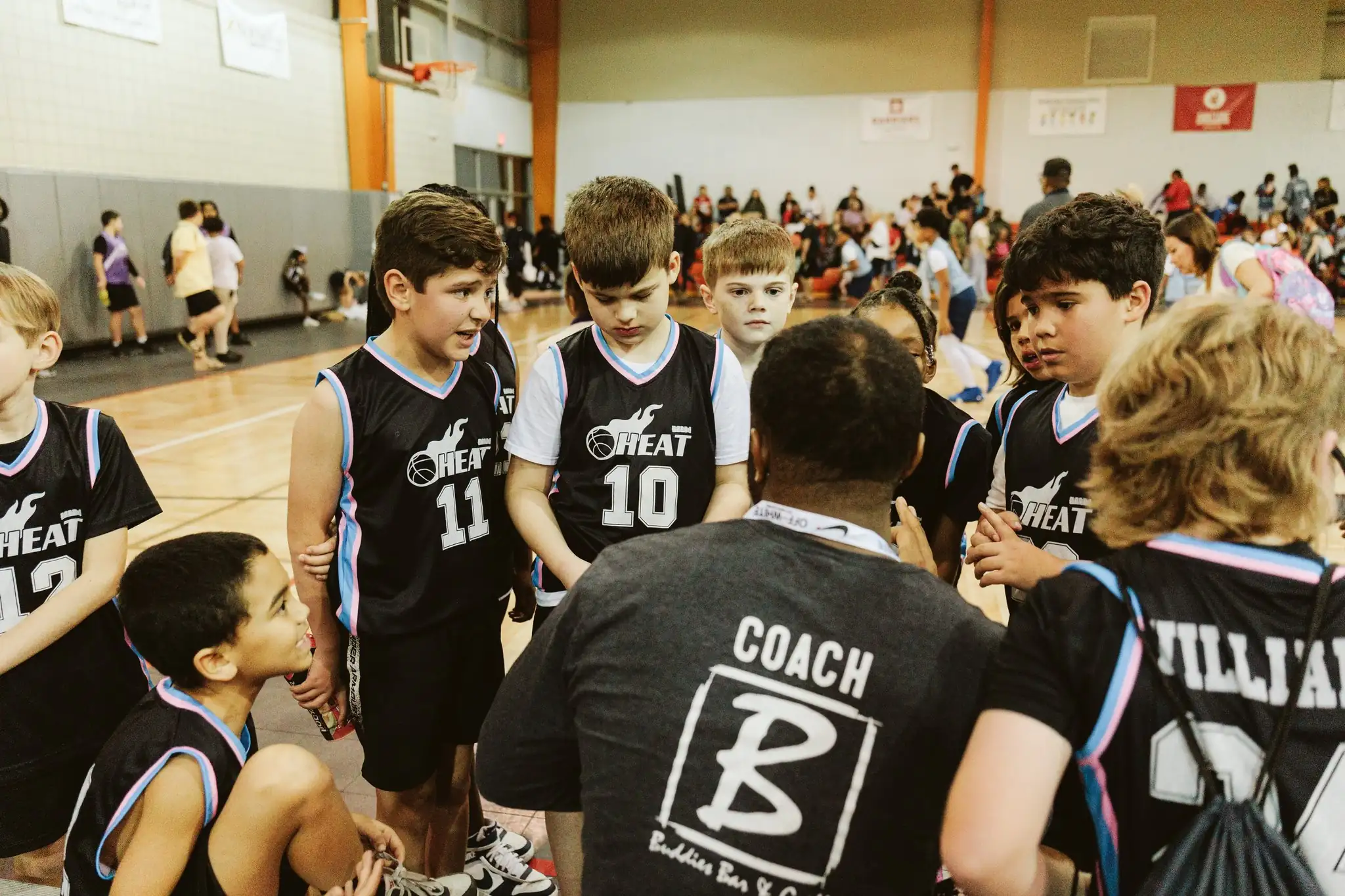Youth Zemurray Sports Program basketball team in black jerseys gathered around their coach in a gymnasium.