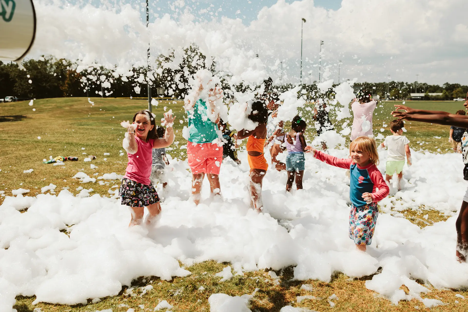 Children playing and throwing foam bubbles in a grassy outdoor field rental at H.A.R.D. #1 on a sunny day.