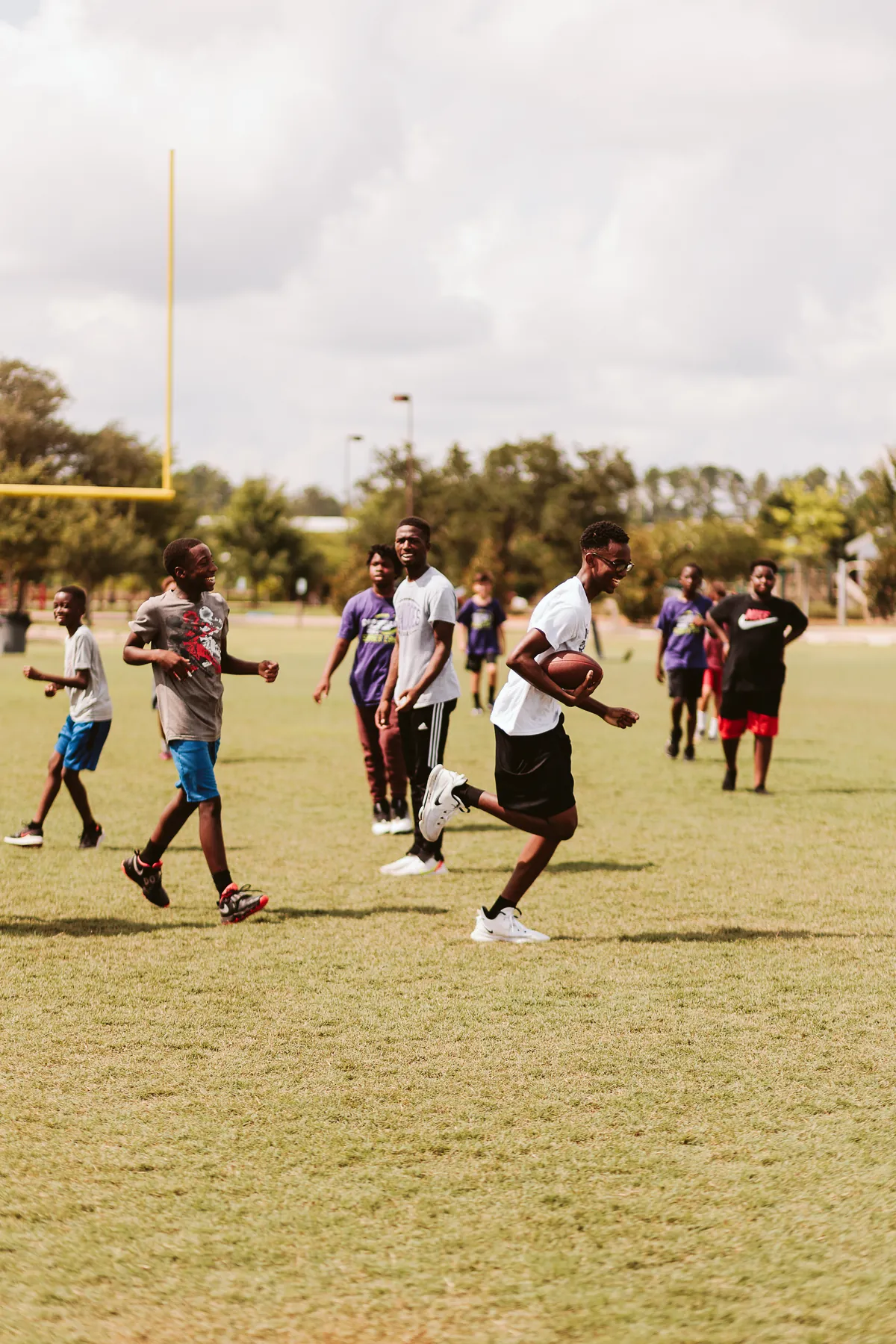 Group of boys playing football outdoors on a grassy field with goalposts and trees in the background.