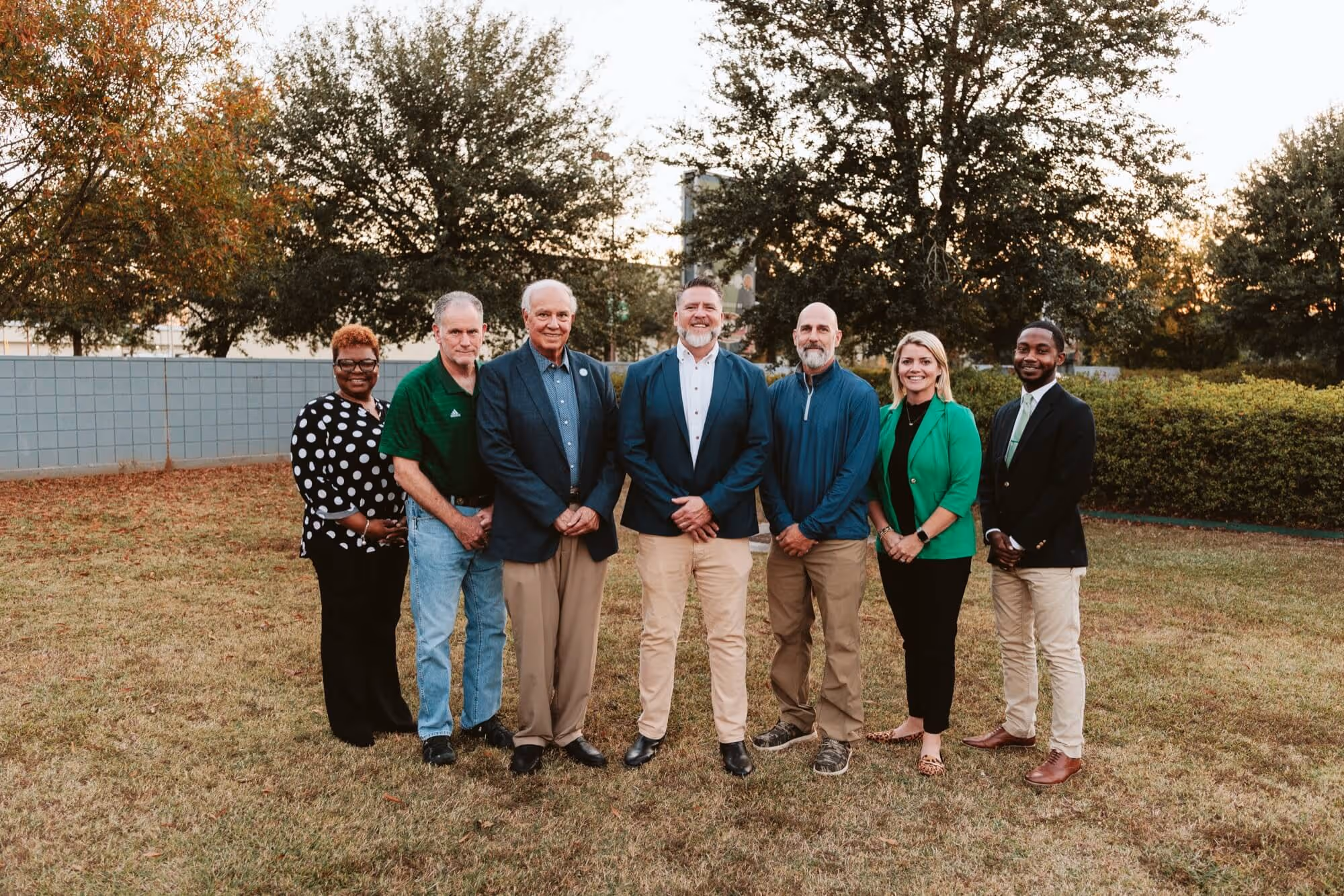 The board of directors for H.A.R.D. #1 professionally dressed standing outdoors on grass with trees and a fence in the background, smiling at the camera.