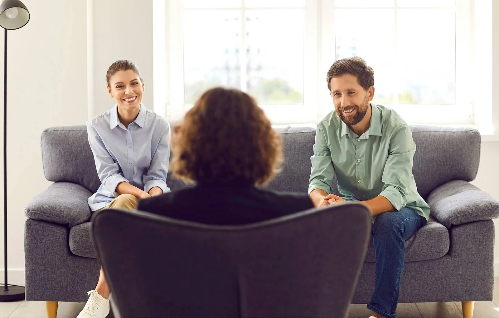 Young couple sitting on a couch, smiling and engaged in conversation with a professional during a counseling session.