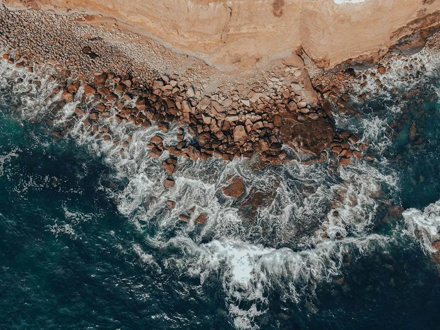 Aerial view of rugged San Diego coastline with turquoise waves crashing against rocky shore.