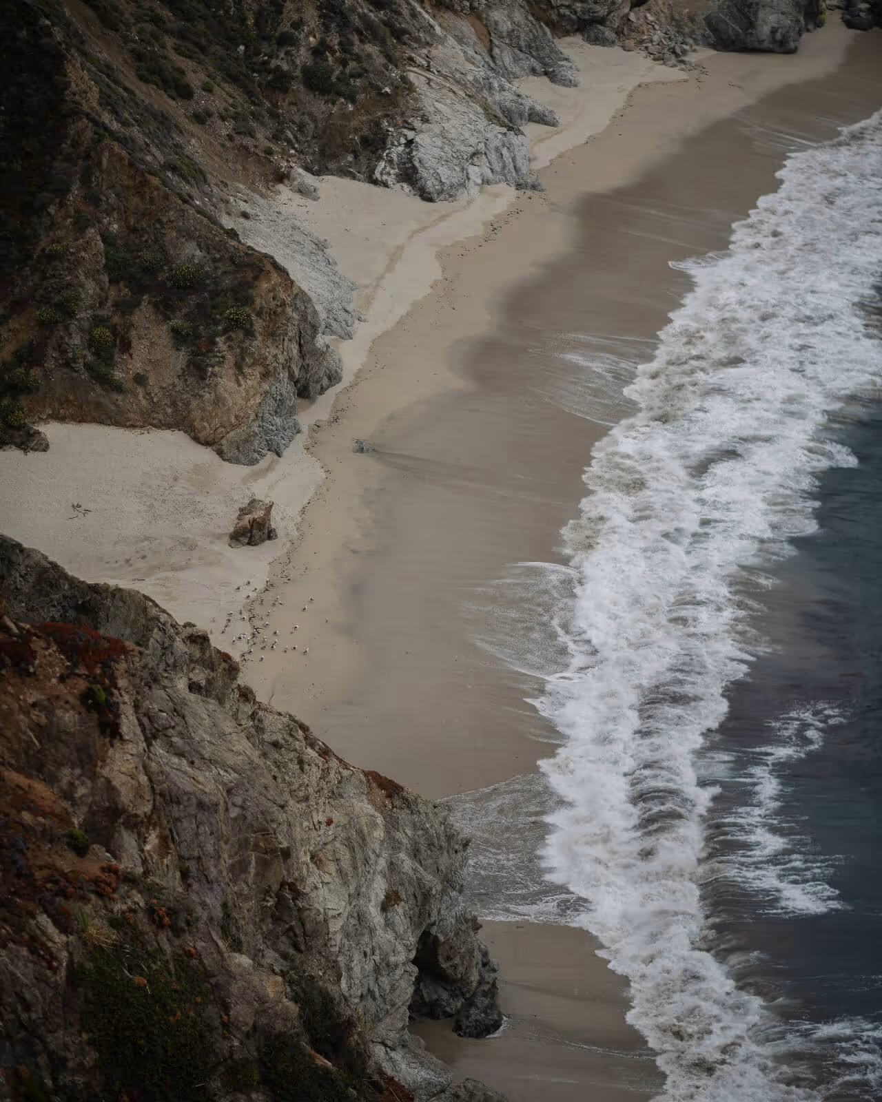 Ocean waves hit sandy beach under rocky cliffs.