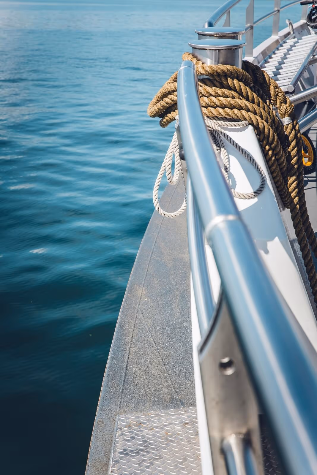 Boat deck with coiled ropes and metal railings overlooking calm blue ocean water.
