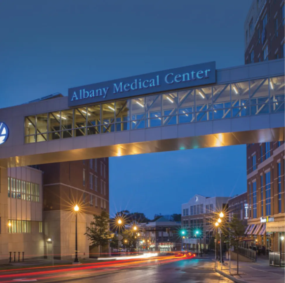 Illuminated Albany Medical Center sign spanning across the street via modern pedestrian bridge.