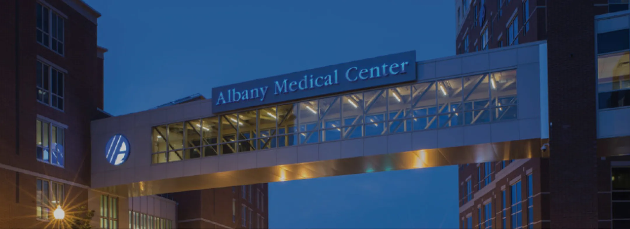 Illuminated skybridge connecting buildings at Albany Medical Center during twilight.