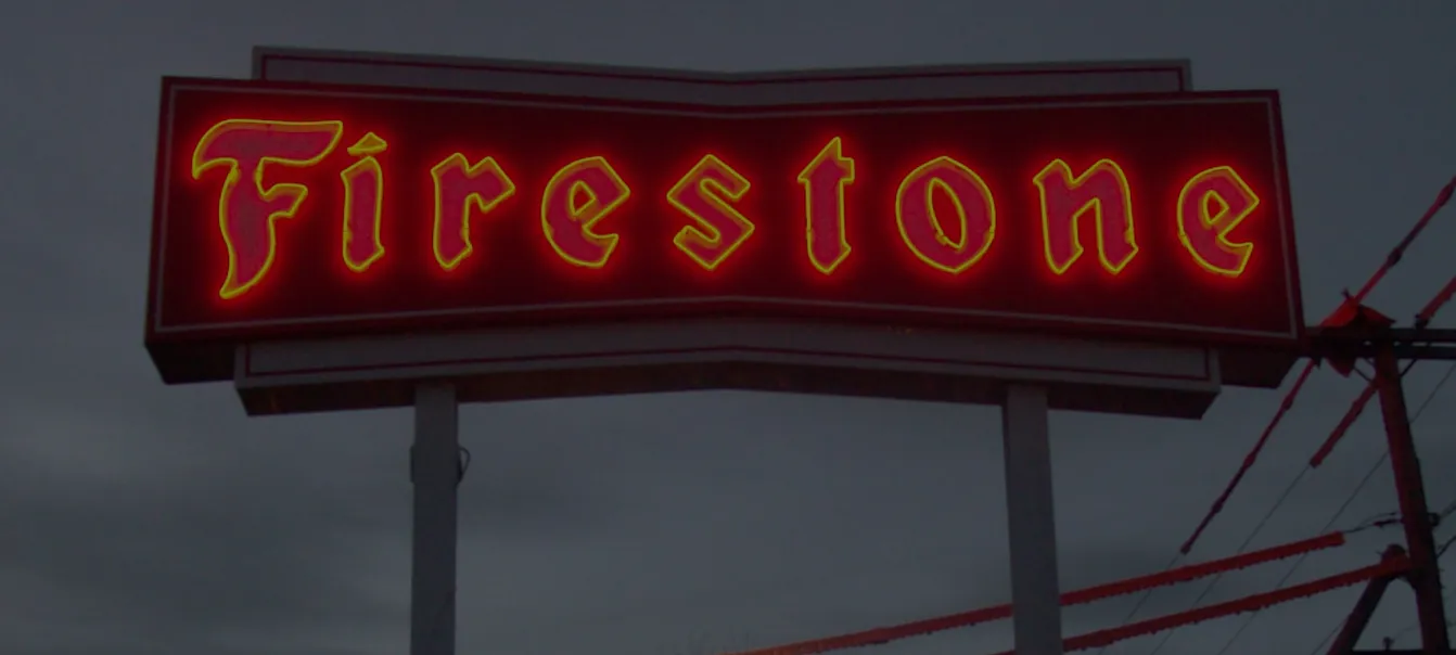 Red and yellow glowing Firestone sign illuminated against a dusky sky