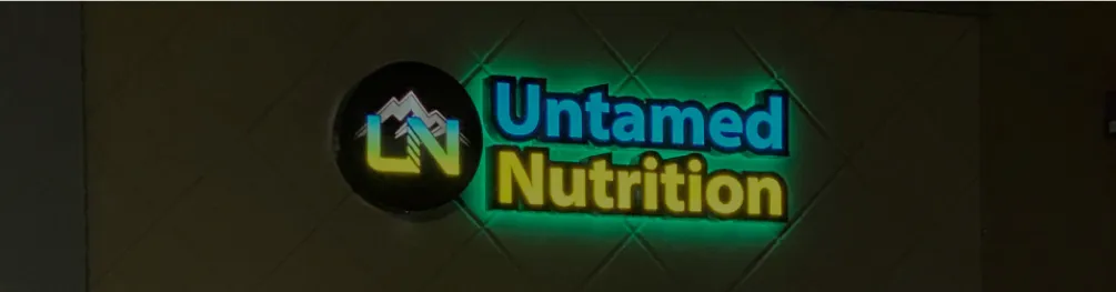 Illuminated logo signage for Untamed Nutrition on a tiled retail storefront.