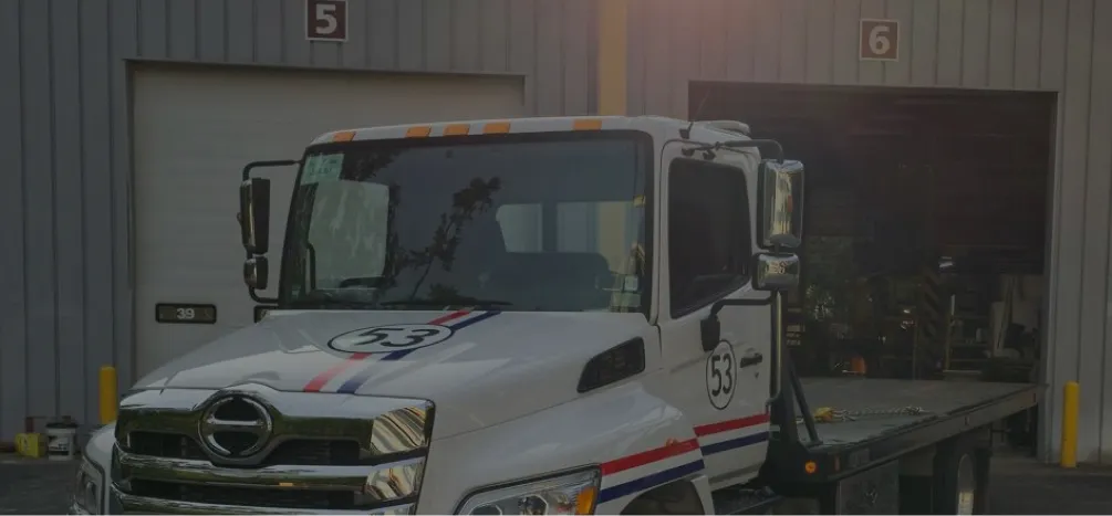 White delivery truck with racing stripes and number 53, parked outside commercial garage.