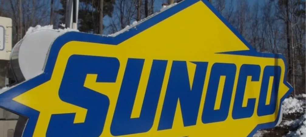 Close-up of Sunoco gas station logo on outdoor sign with winter trees in background