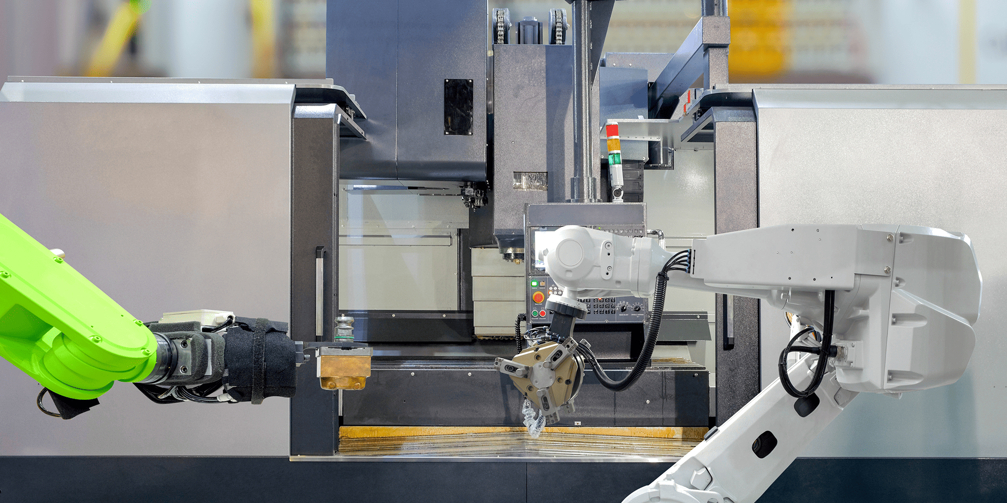 Two robotic arms working on a machine in an industrial setting.