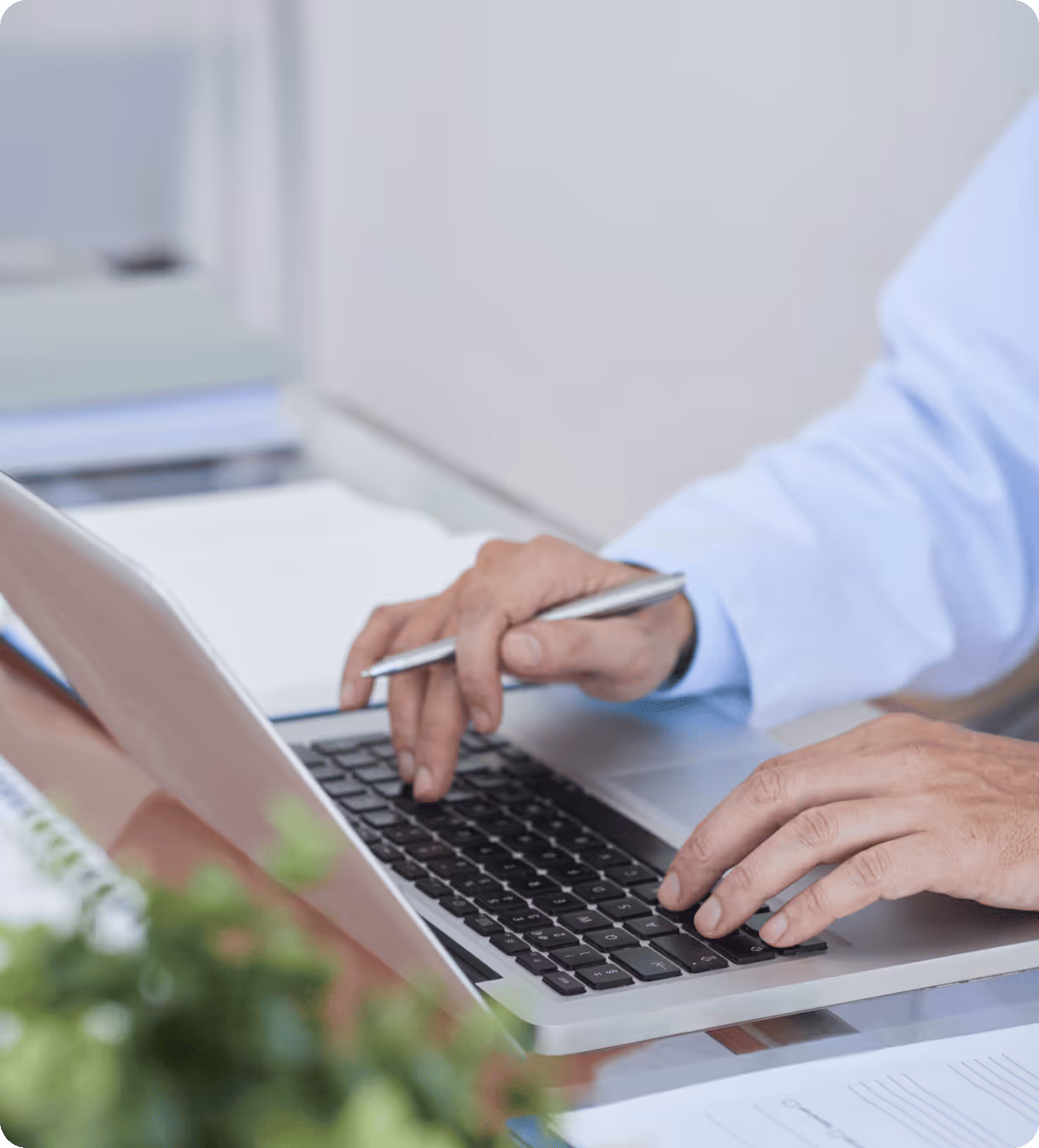 Person typing on laptop with pen in hand.