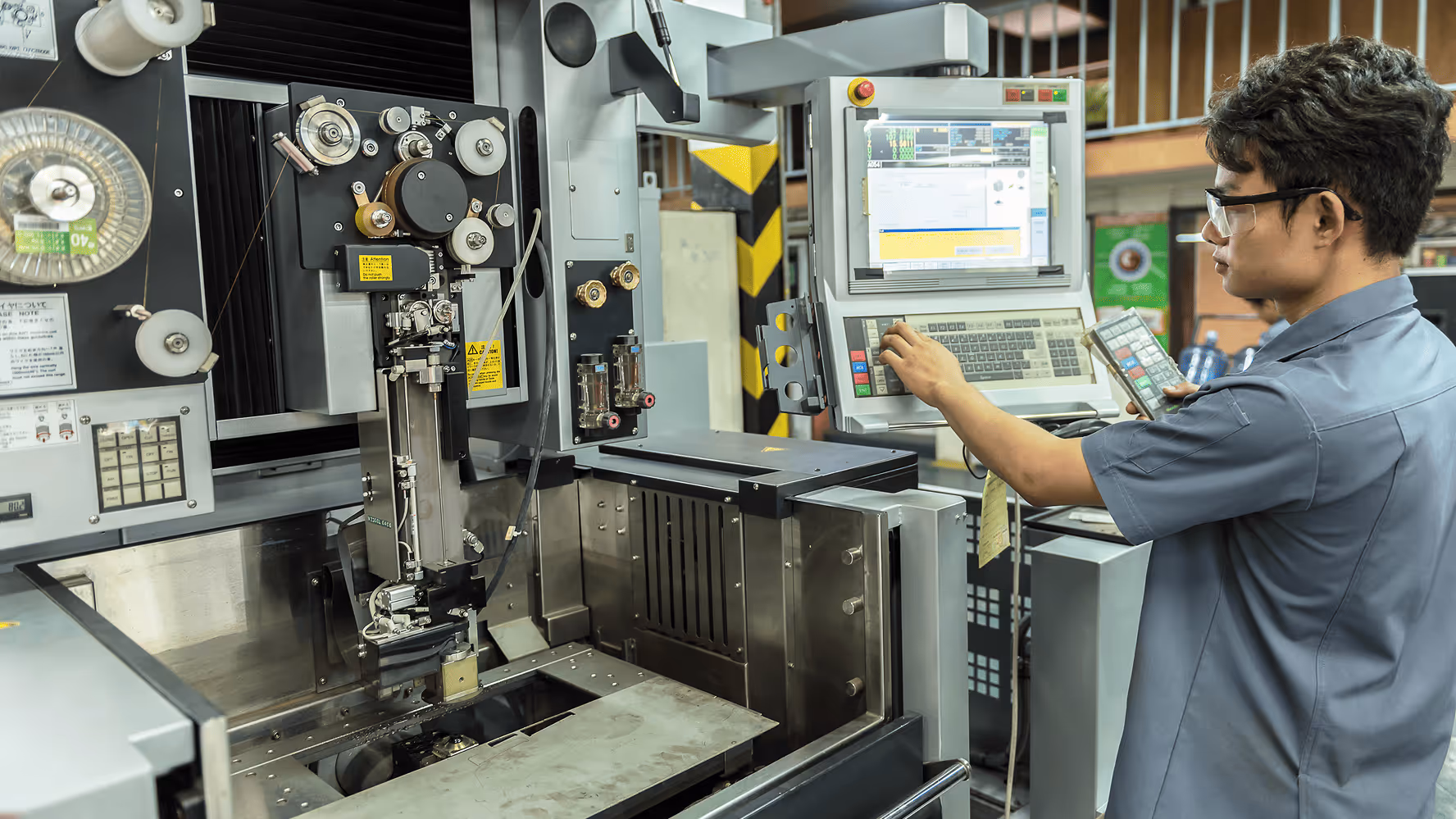 Worker adjusting an EDM machine with a control panel.