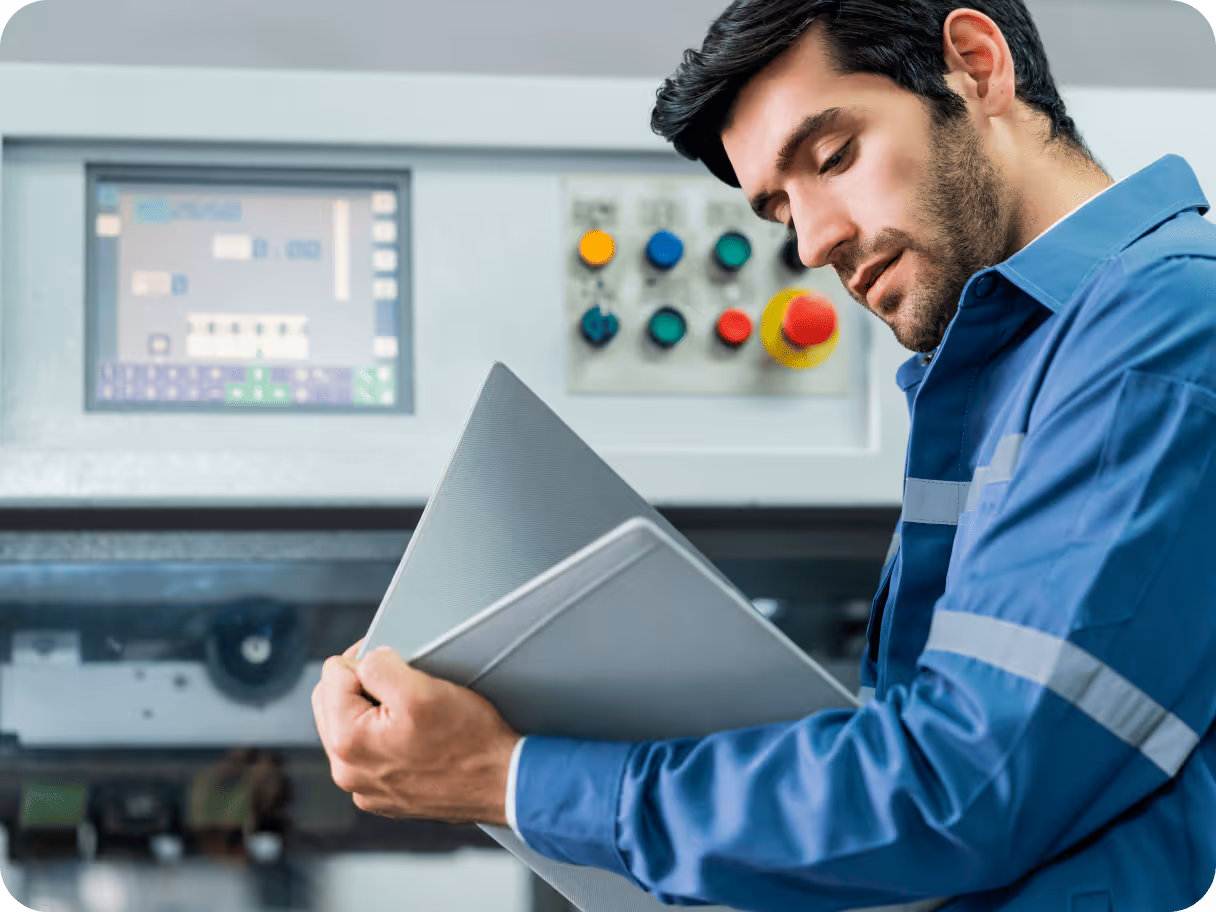 Technician holding documents while inspecting a machine control panel with buttons and a digital display.