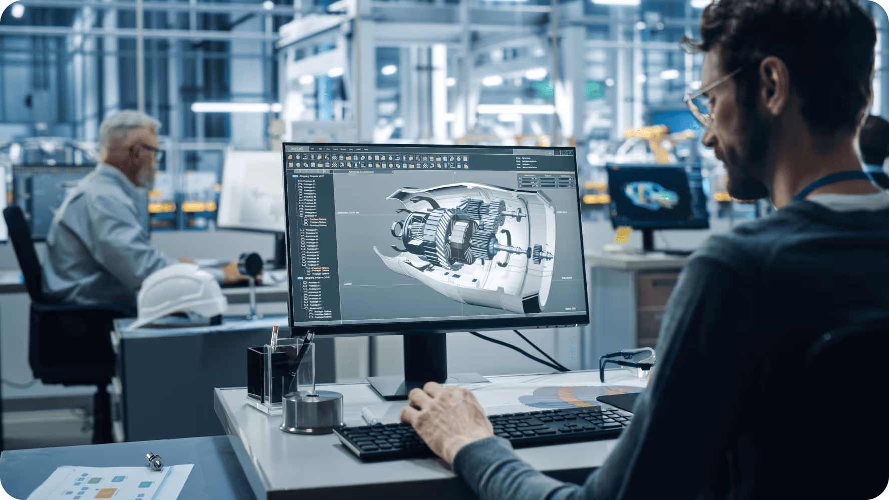 Engineer working at a computer with a detailed 3D CAD model of a machine component in an industrial office.