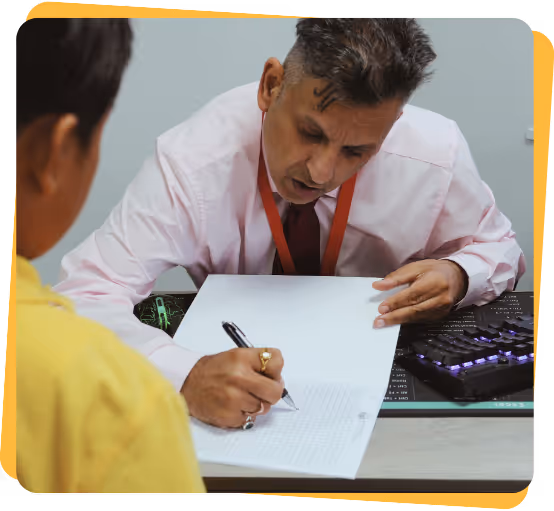 A tutor leans over a desk, marking a student's paper to check their answers.