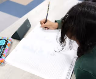 Student writing on graph paper with tablet and pencil case during 11 Plus prep.