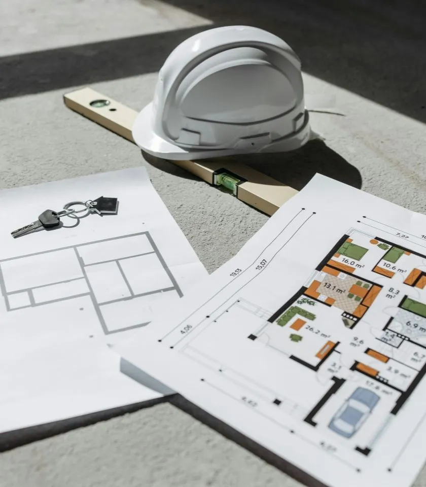 Floor plans, house keys and a hard hat on a desk
