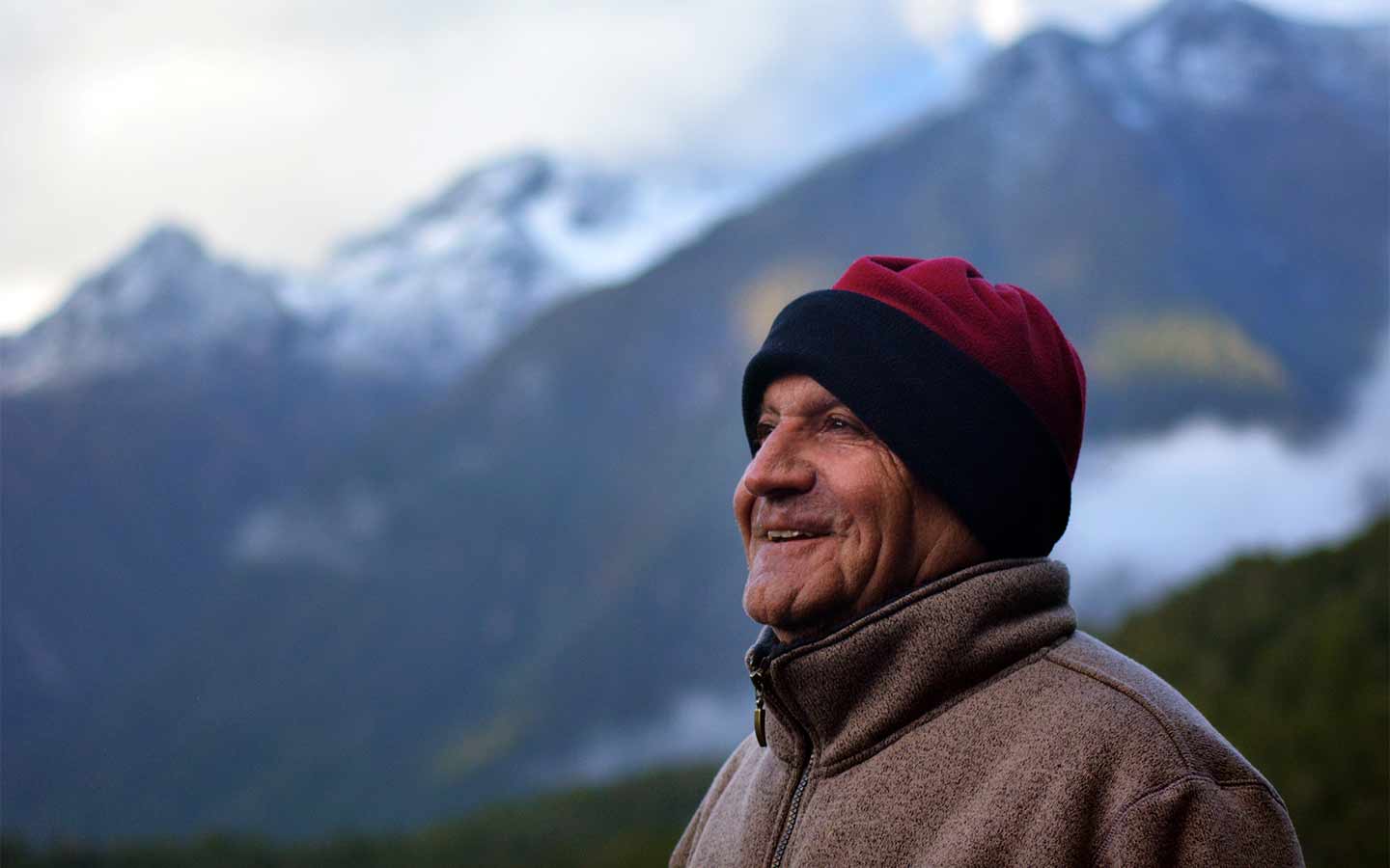 Kiwi missionary smiling in New Zealand mountains, wearing a warm outdoor beanie and jacket. OM New Zealand