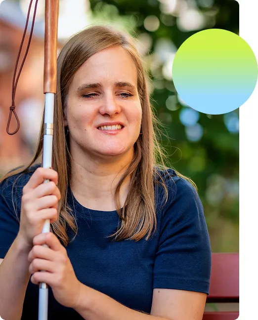 Blind woman sitting on a bench outside with a walking cane and smiling