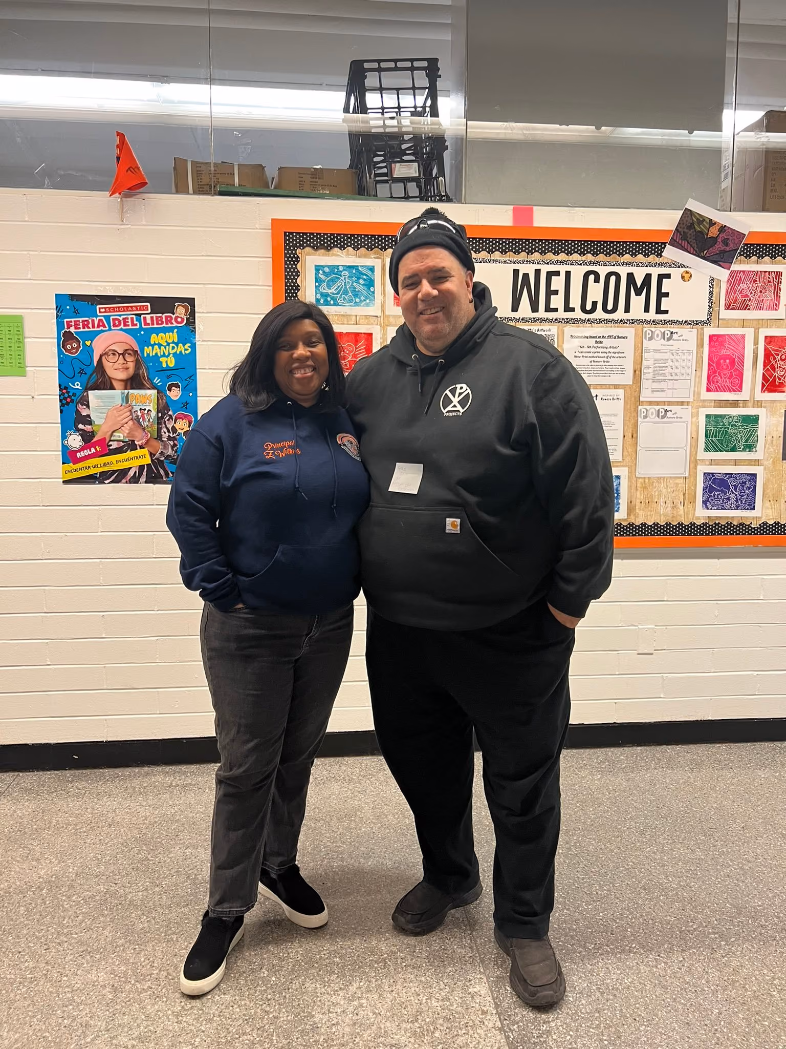 Two staff members smiling in front of school welcome bulletin board