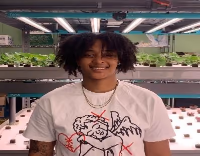 Student smiling in front of indoor hydroponic growing shelves
