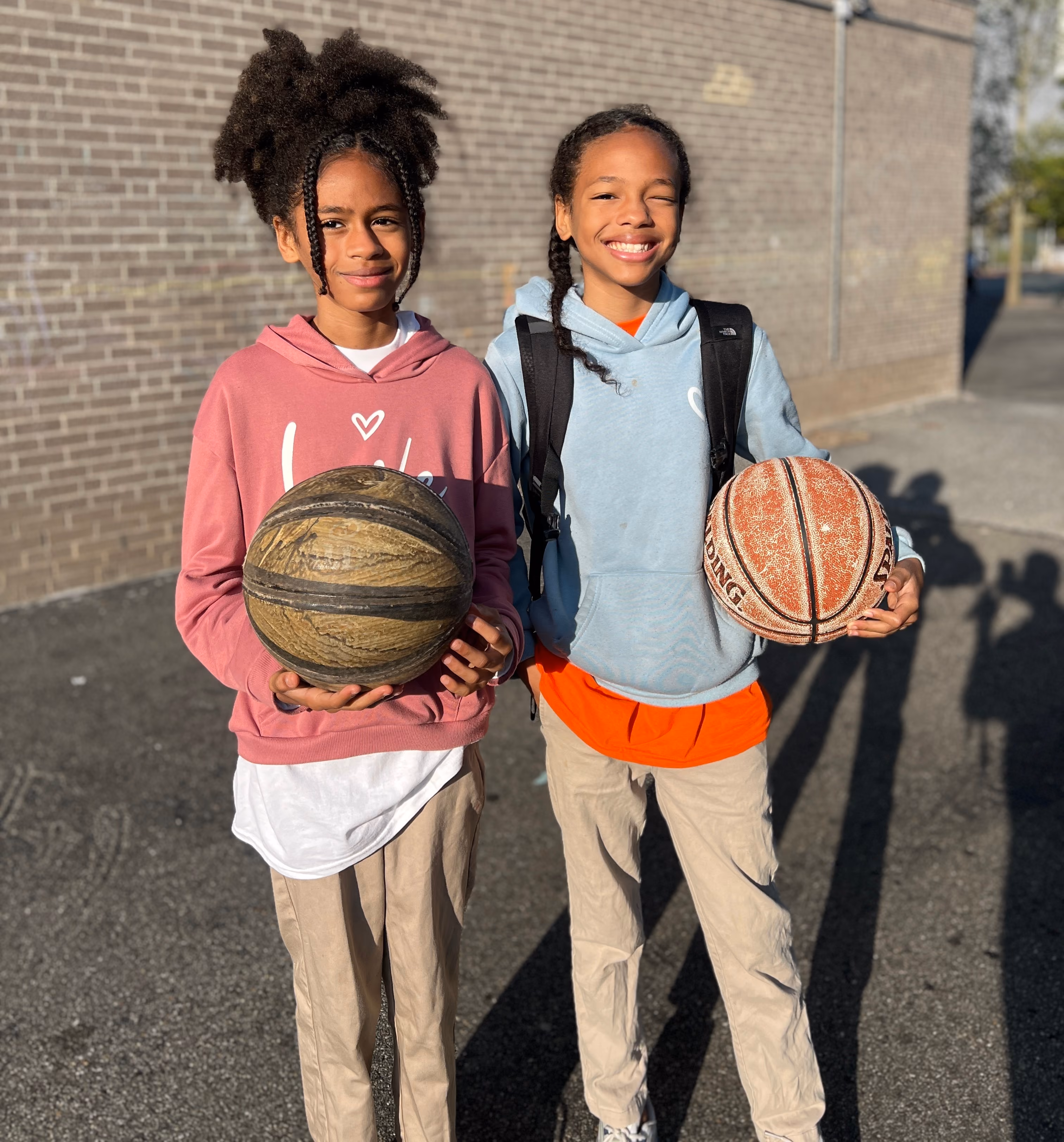Two students smiling and holding basketballs on school grounds