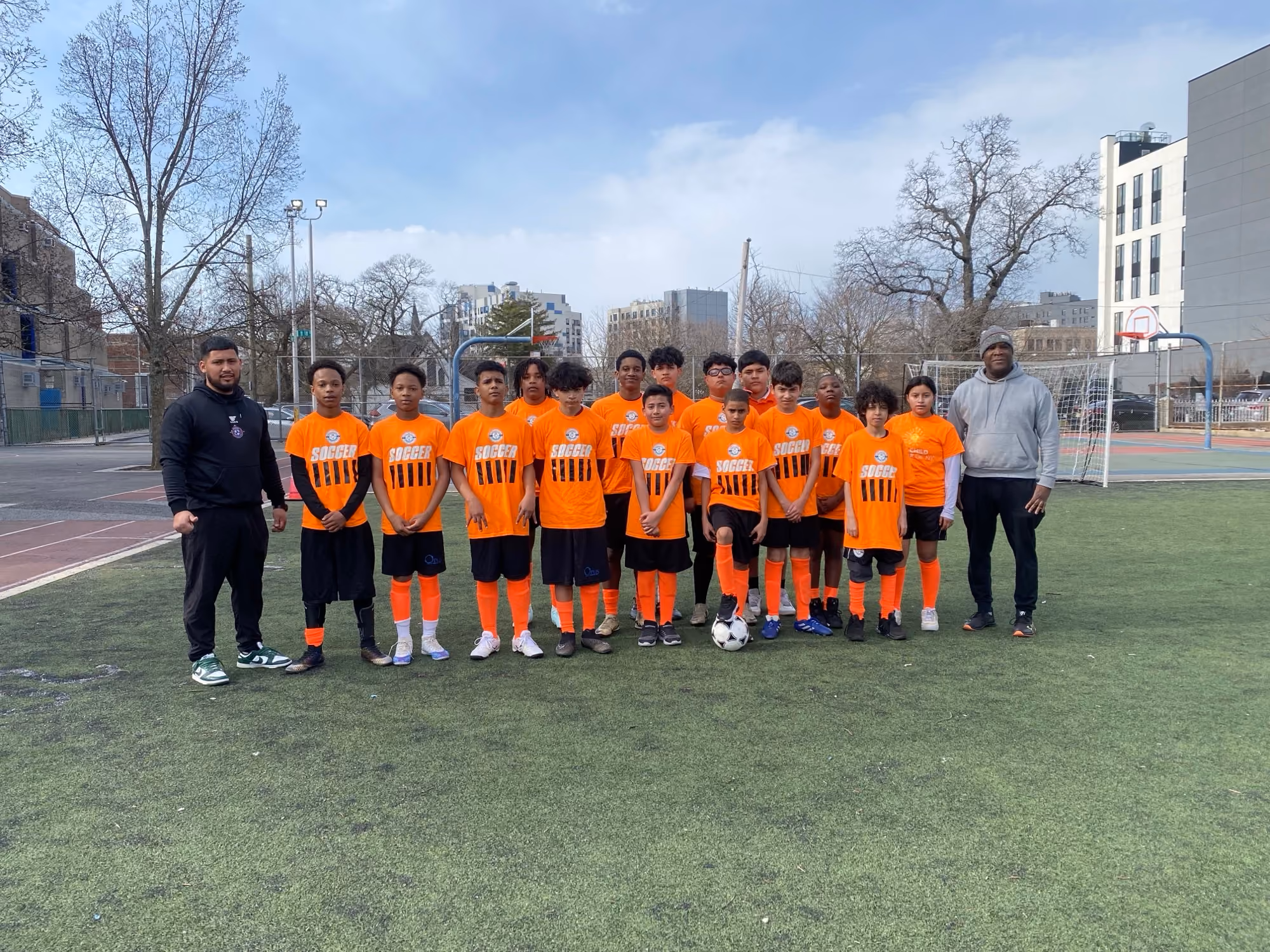 Student soccer team in orange jerseys posing with coaches on field