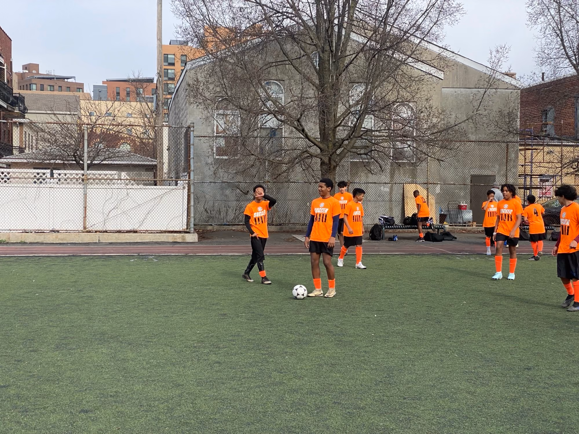 Students in orange jerseys practicing soccer on outdoor turf field